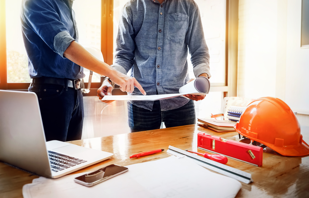 A young engineer pointing blueprint and use laptop to explaining the design to the foreman,