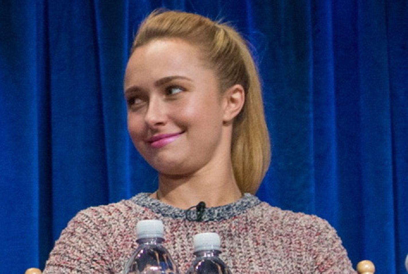 Hayden Panettiere in sweater and pink lipstik looking at side and smiling at blue background - 2013