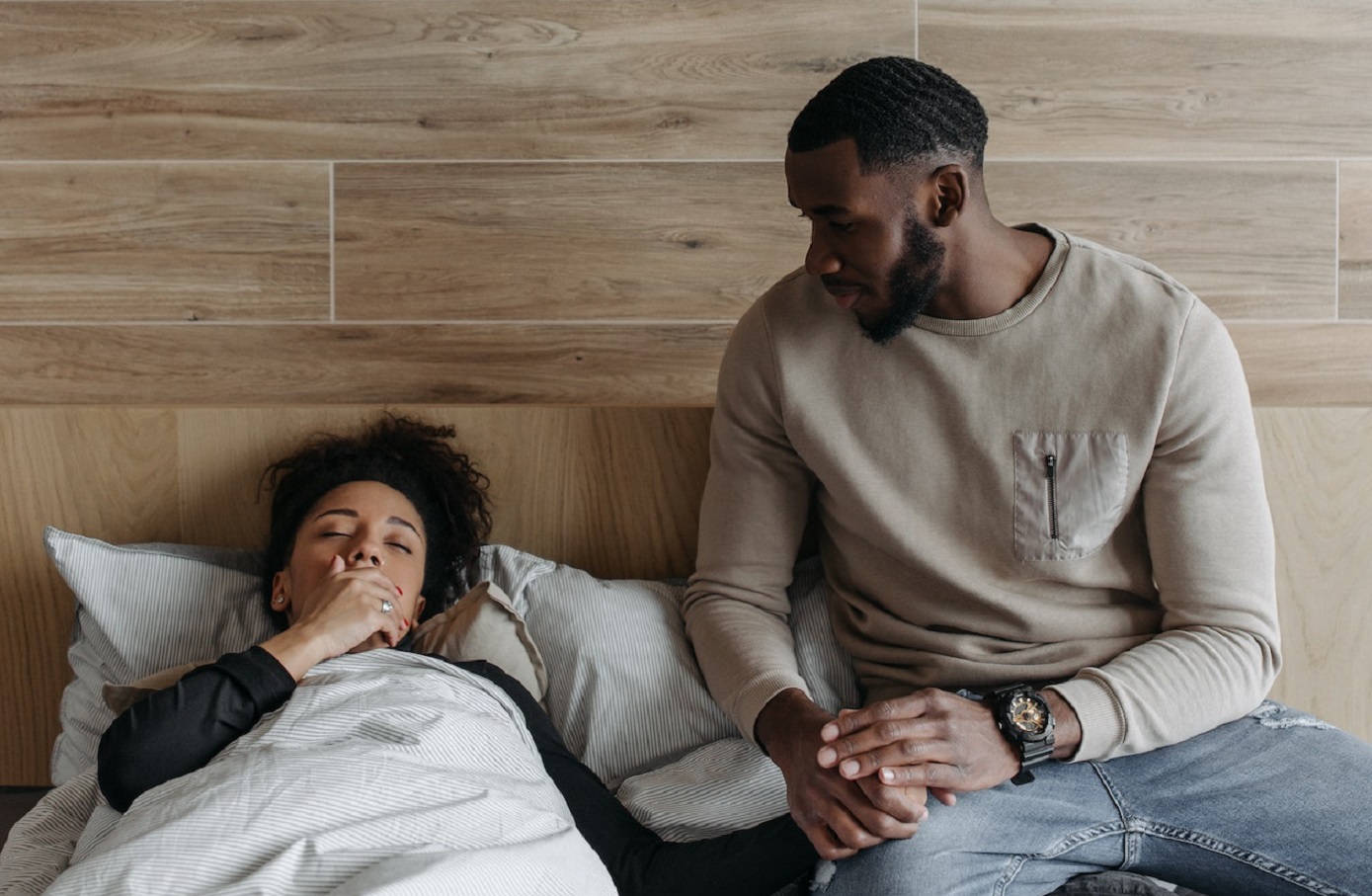 Black man holding hand to a black woman who is feeling sick.