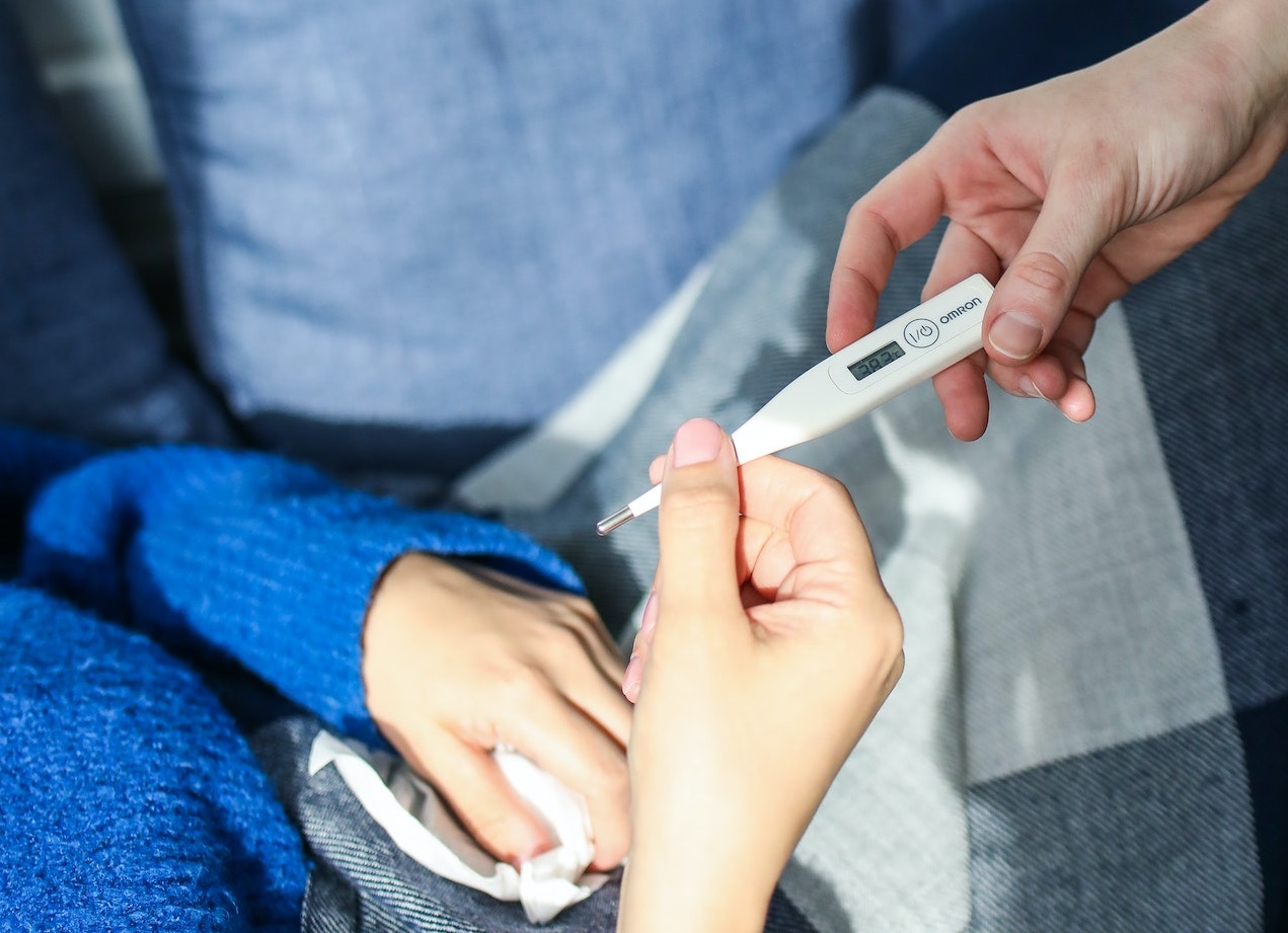 Woman with oral thermometer in her hand wearing blue shirt.