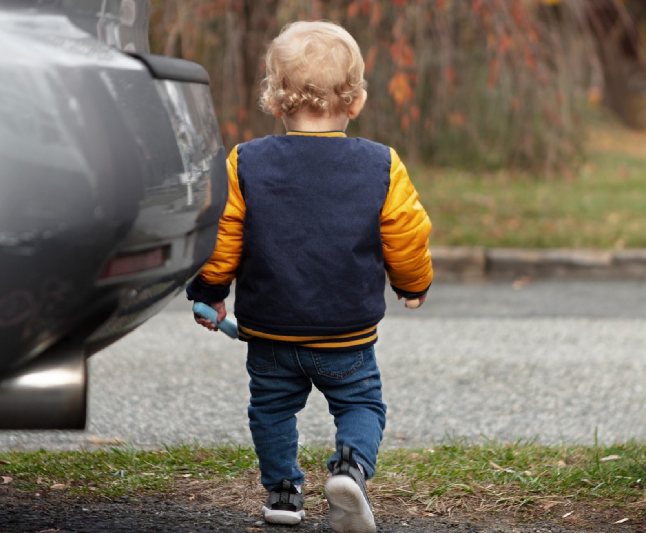 Small kid standing by the grey car turned with his back.