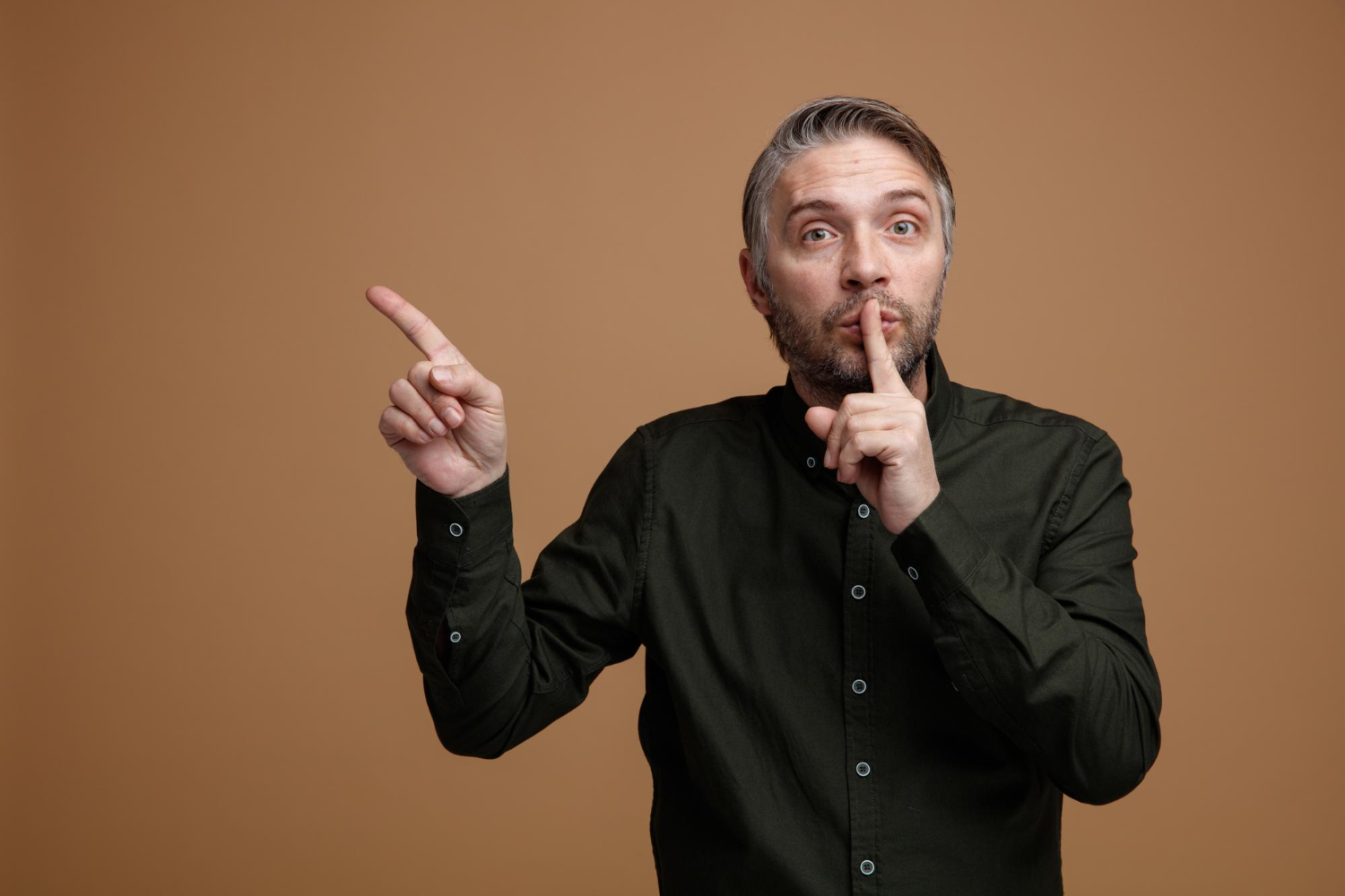 Man with beard wearing black shirt making silence gesture.