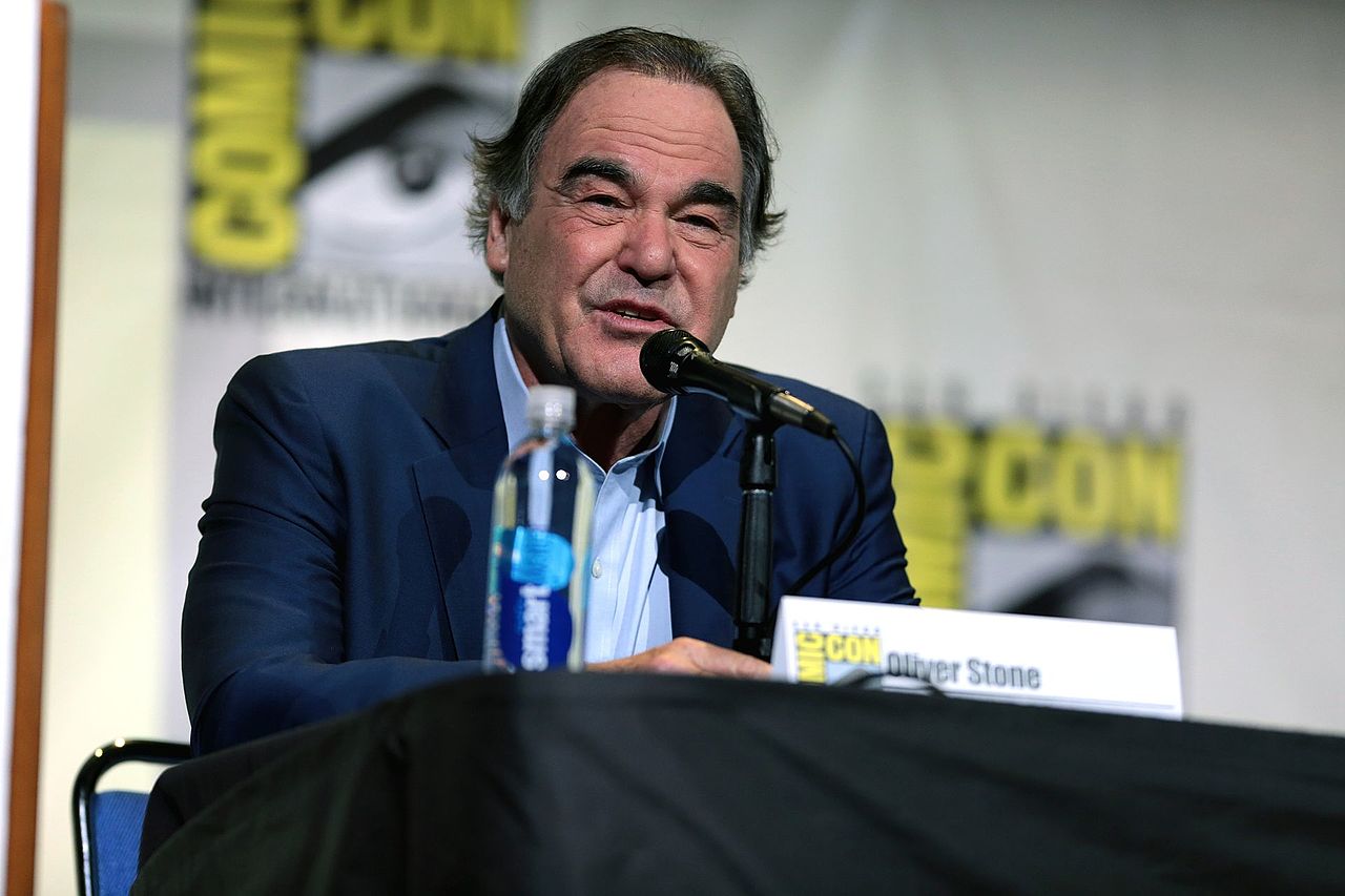 Oliver Stone in suit sitting at table