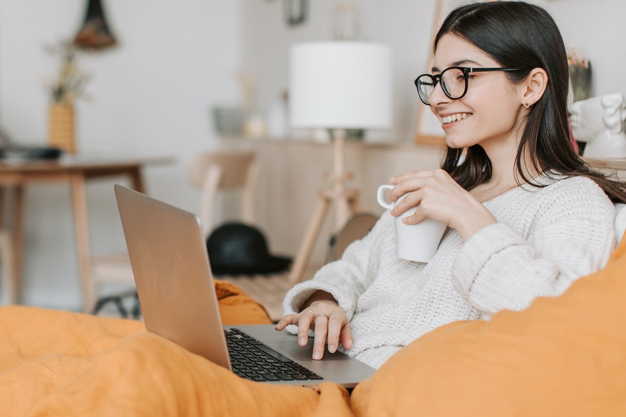 Woman seating on the bed and looking at her laptop.
