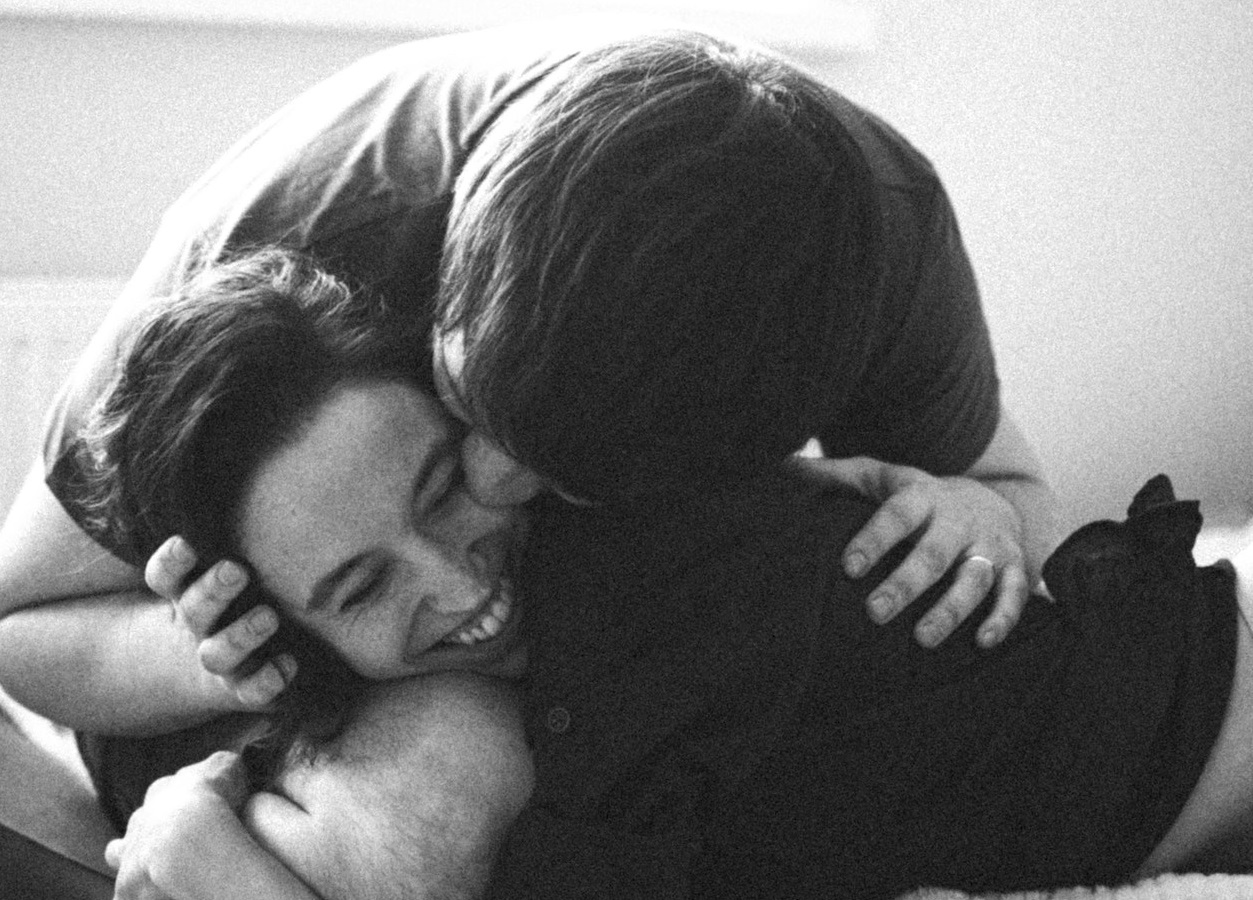 B&W photo of man kissing his girlfriend laying on the bed and smiling.