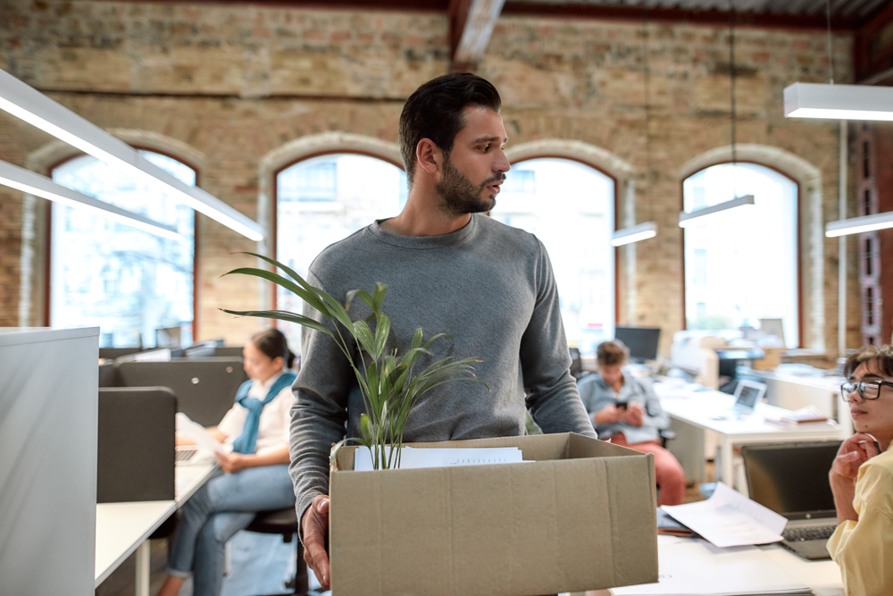 Upset man in casual wear holding box with things and leaving the office
