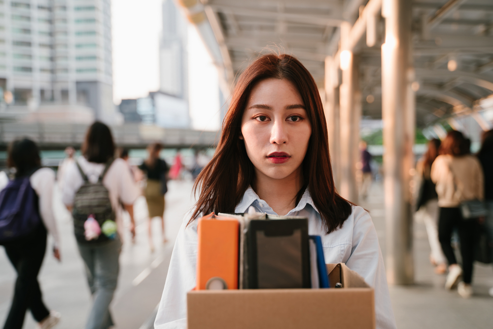 Portrait of young Asian woman holding box of items after being laid off from job