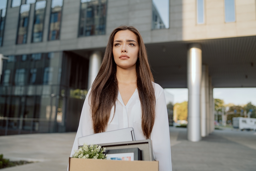 Sad woman in front of office building with belongings just quit job or is fired