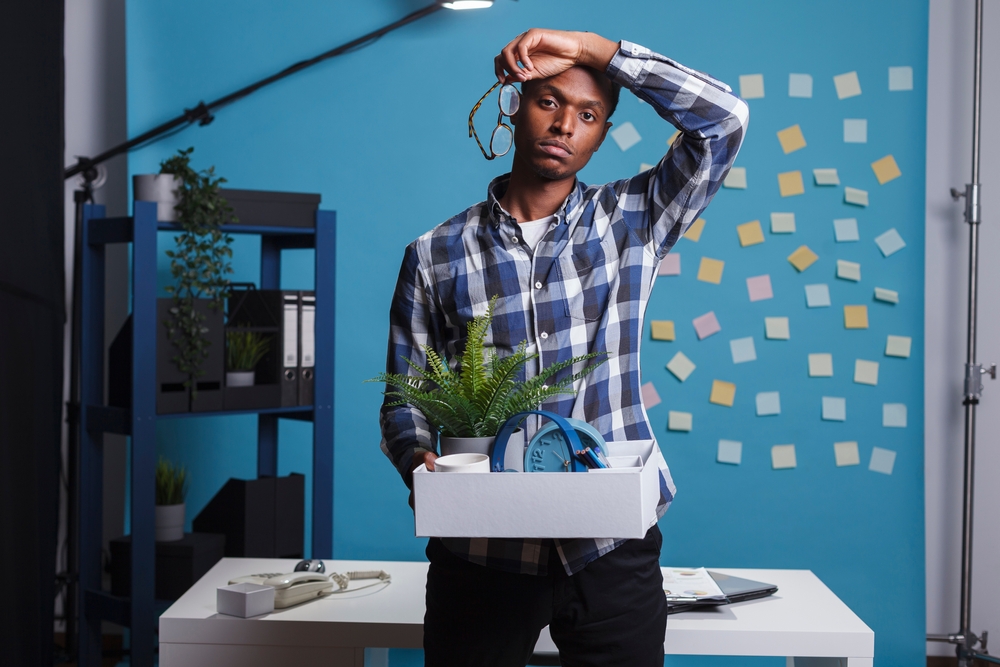 Man getting fired and packing office things to leave job carrying belongings in flannel shirt