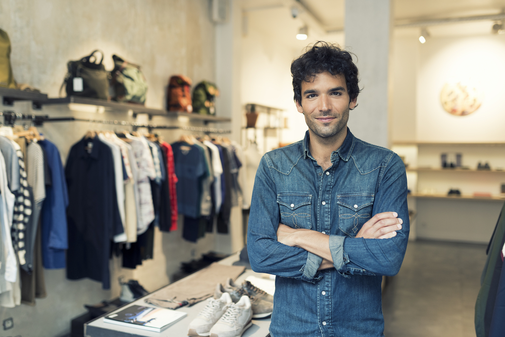 A male employee in clothing store with crossed arms and a day old beard wearing a denim shirt