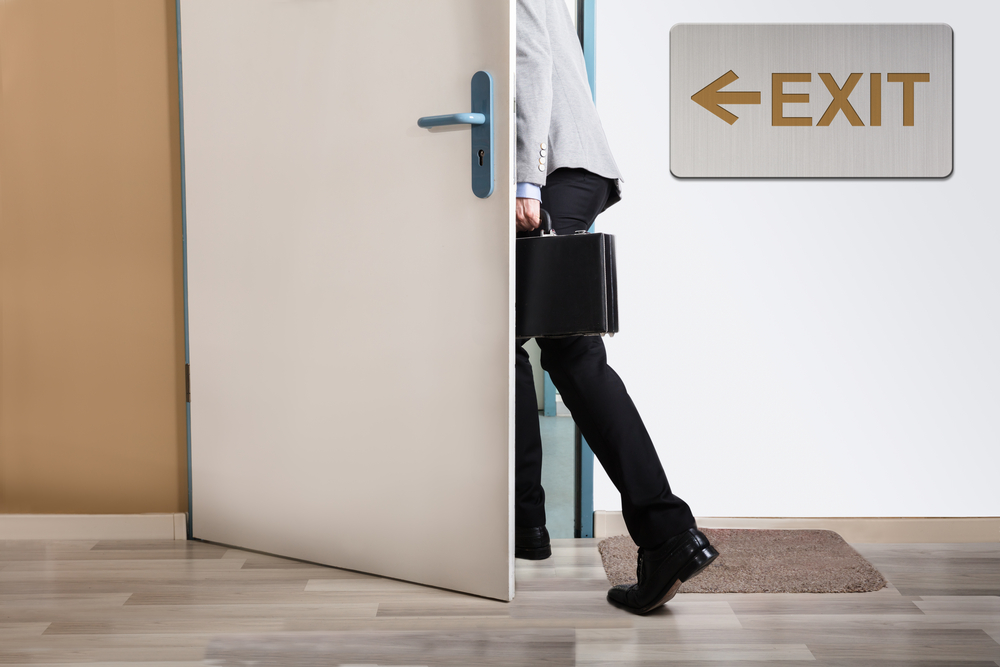 Businessperson Walking Out With Exit Sign On Wall