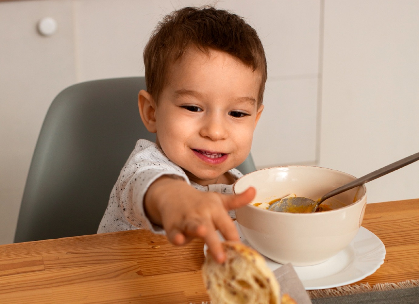 Young kid taking piece of bread from the dinner table.