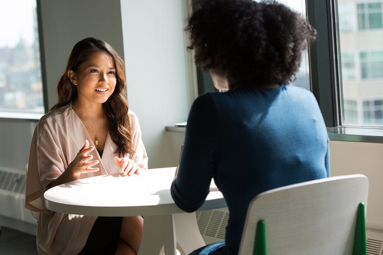 Woman seating on the table with other woman and having a conversation.