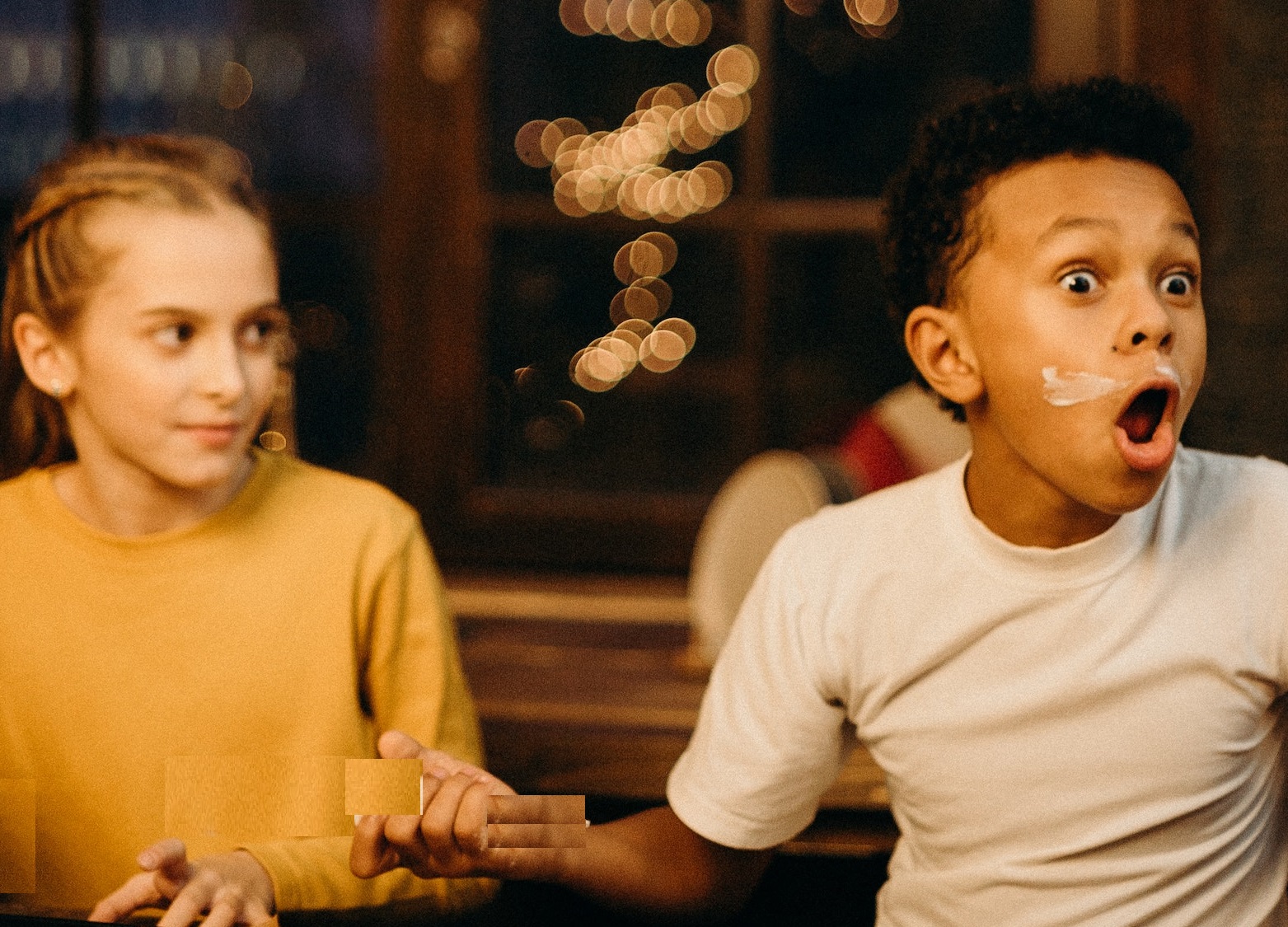 Surprised black kid seating at table next to a girl.