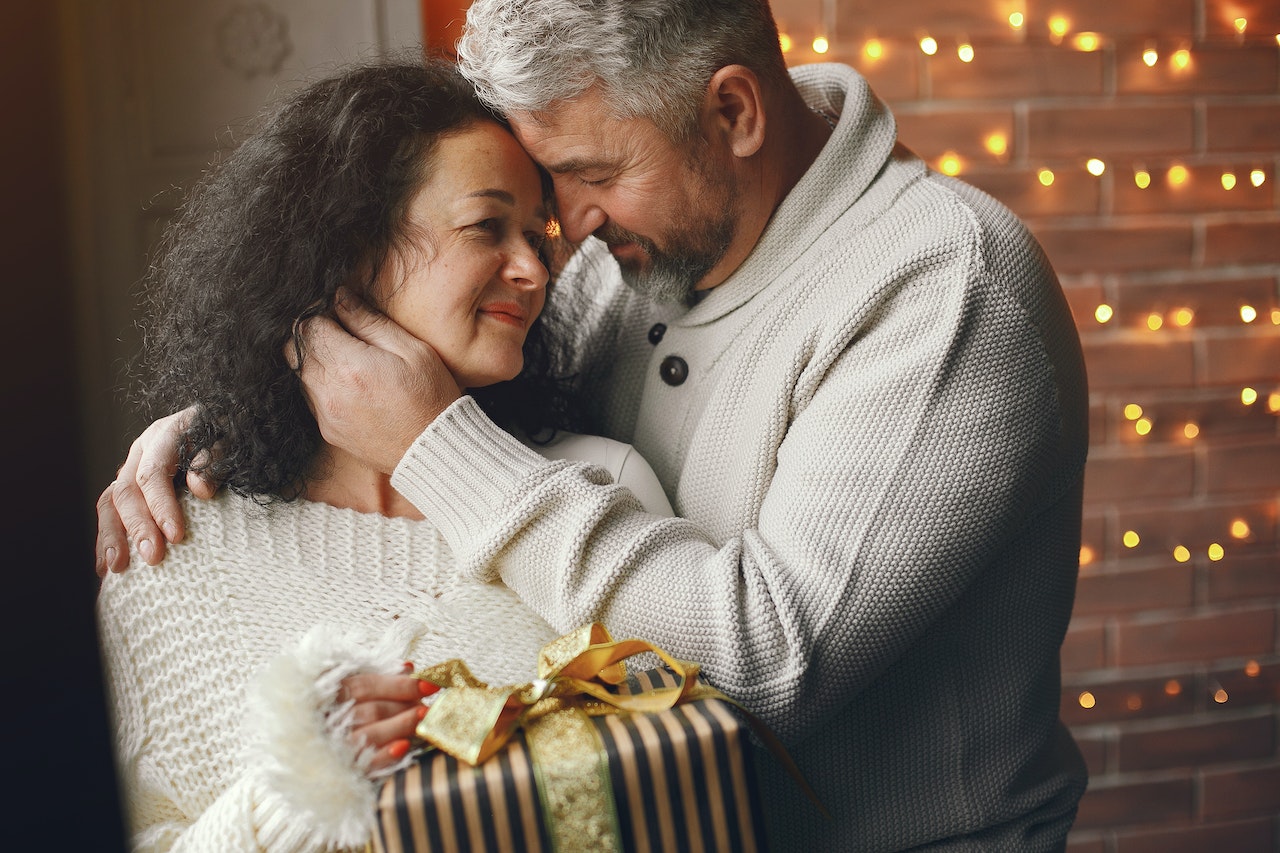 Husband giving a christmas present to his wife and hugging her.