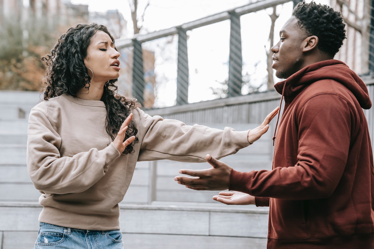 Woman pushing back with hands a black man outside.
