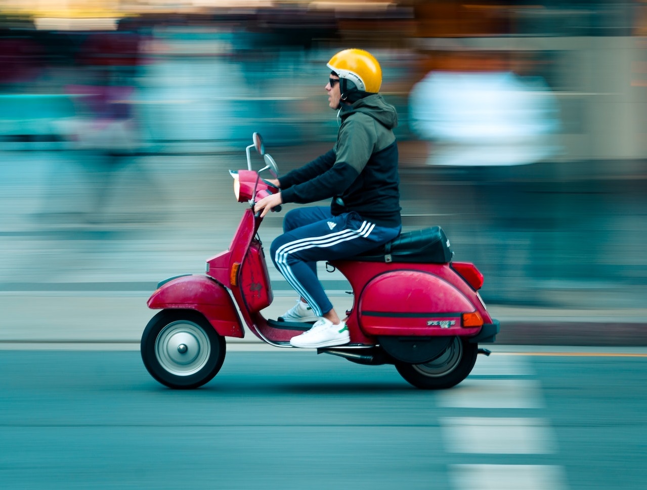 Man wearing yellow helmet is driving a red scooter on the street.