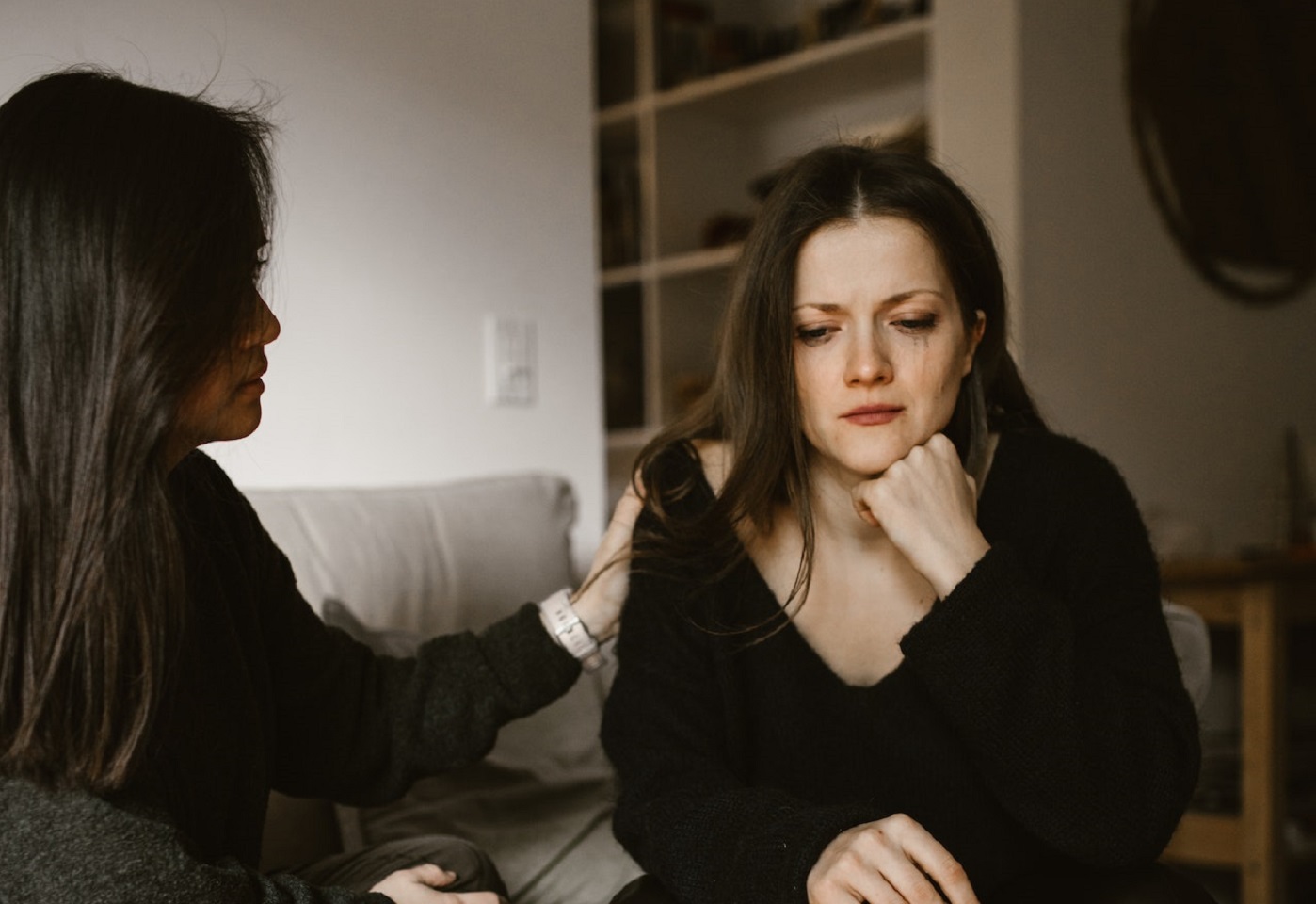 Woman is seating sad on the sofa next to another woman.