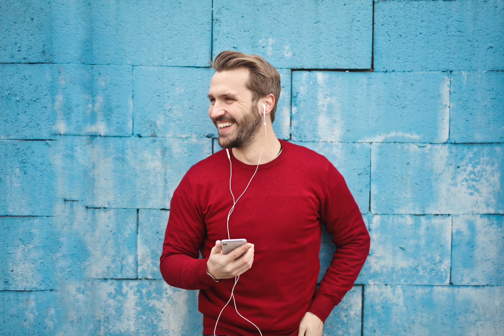 Happy man in red sweater talking on a phone via headset standing in front of a blue wall