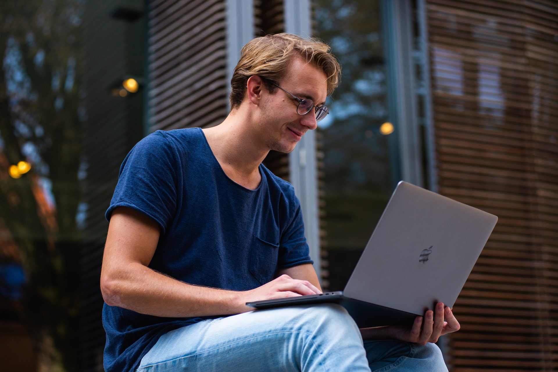 Man in blue t-shirt sitting on a chair working on laptop