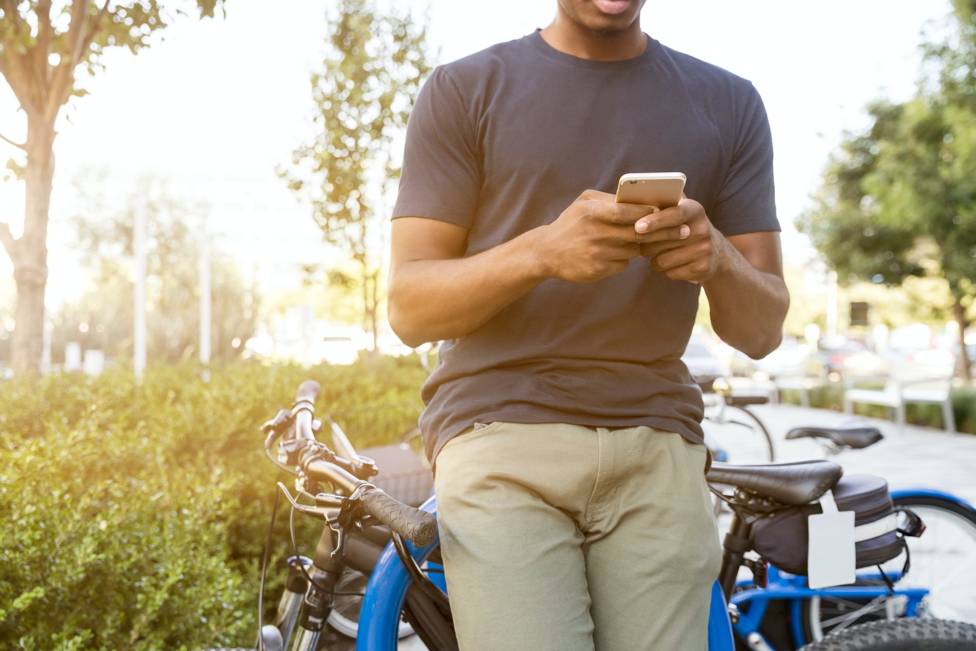 Person leaning on a bike while speaking and typing on phone in gray t-shirt