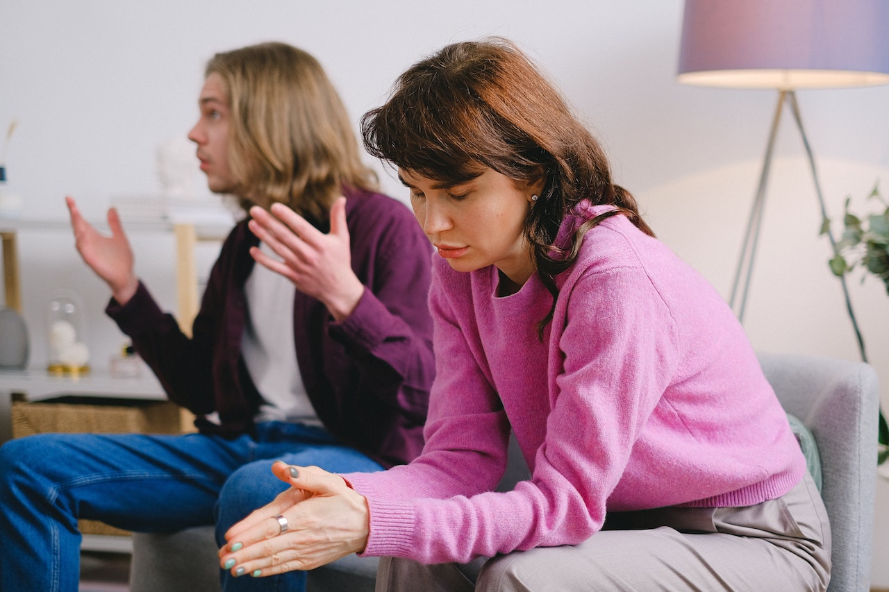 Upset man talking and seating next to a sad woman on the sofa.