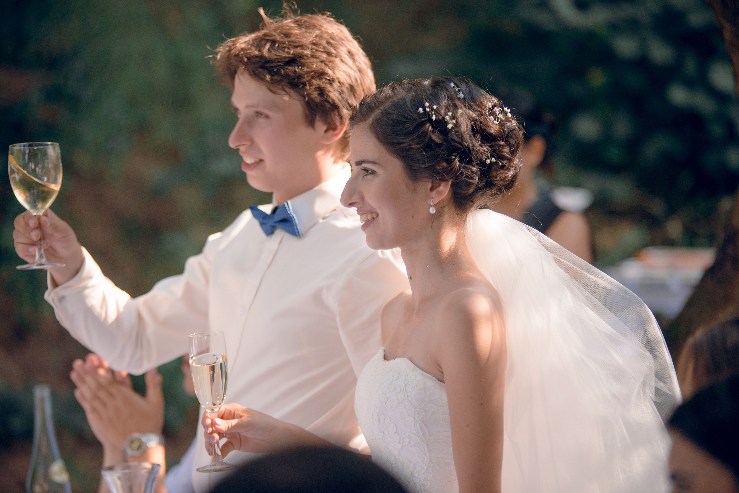 Bride and groom wearing white makes a toast with the guest outside.