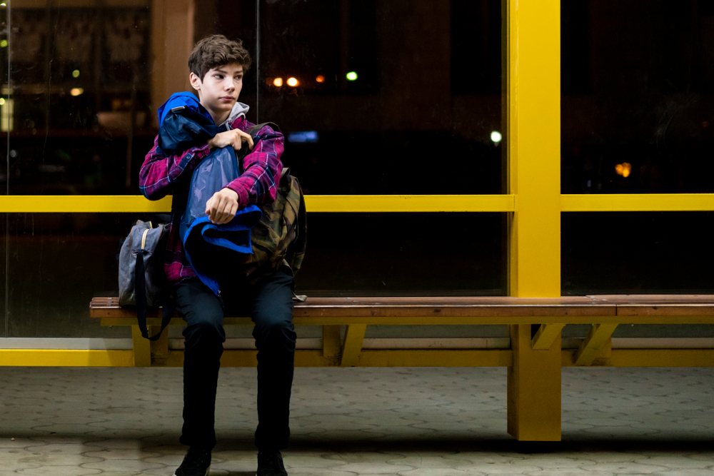 Young man sits on the bus stop bench