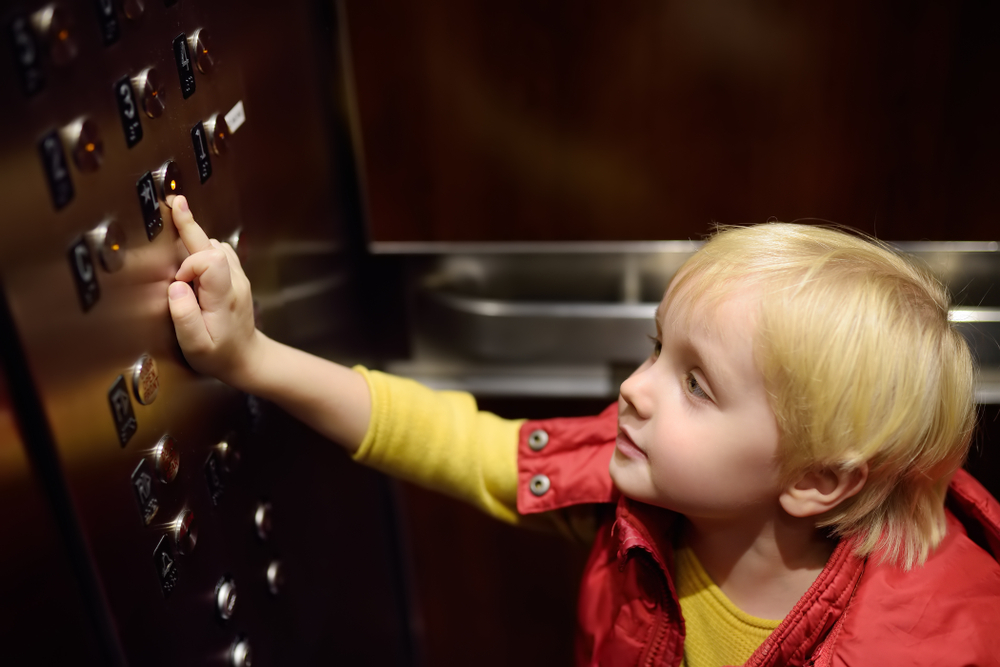 Little boy in red jacket pressing button of an elevator