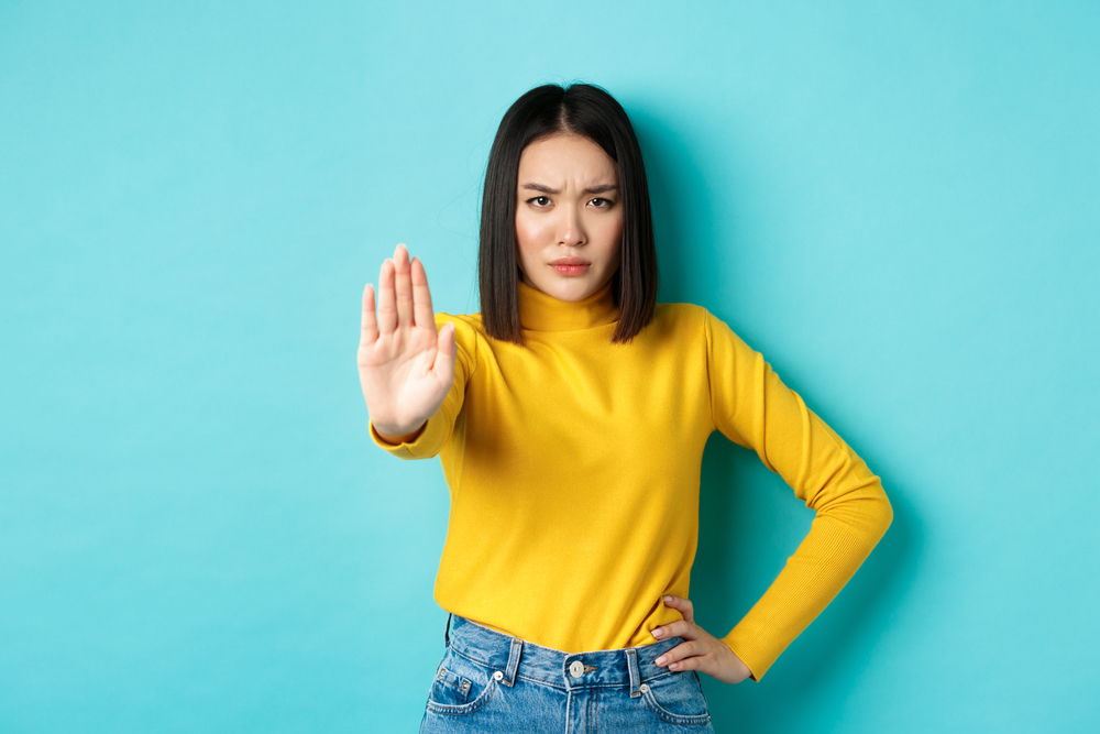 Confident and serious Asian woman tells no, showing stop gesture to prohibit and warn