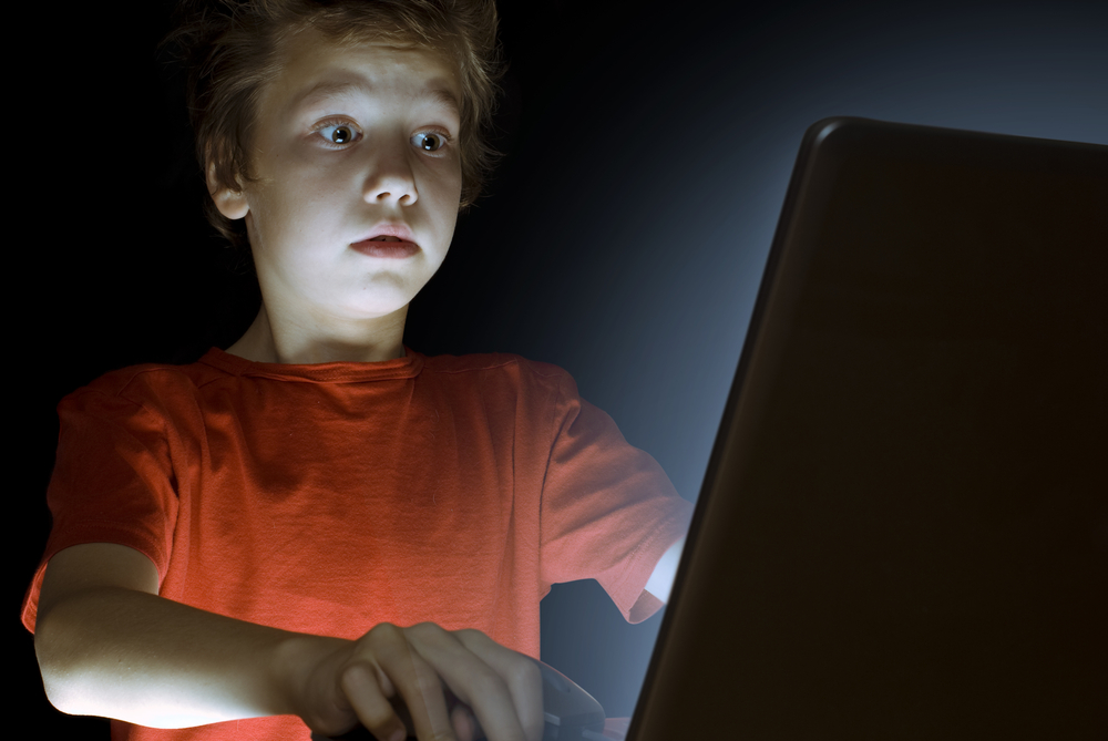 Kid  on a laptop playing a game with shocked face in orange t-shirt