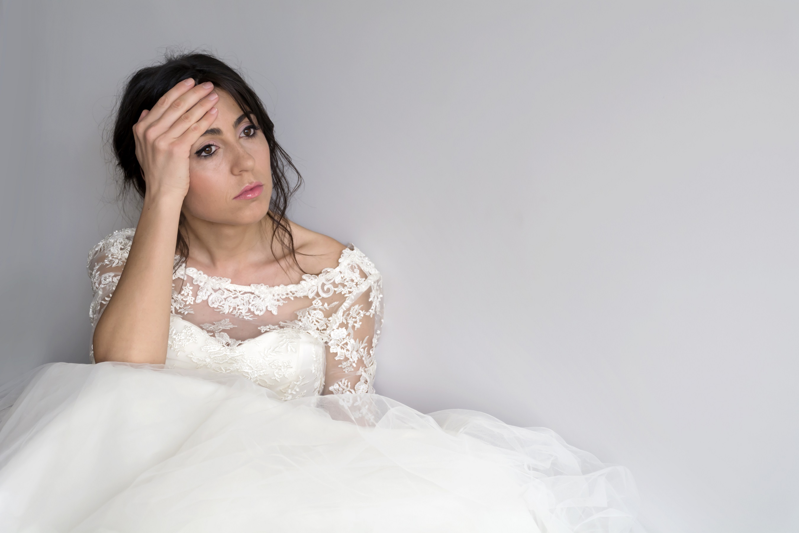 Sad bride wearing wedding dress and holding her head.