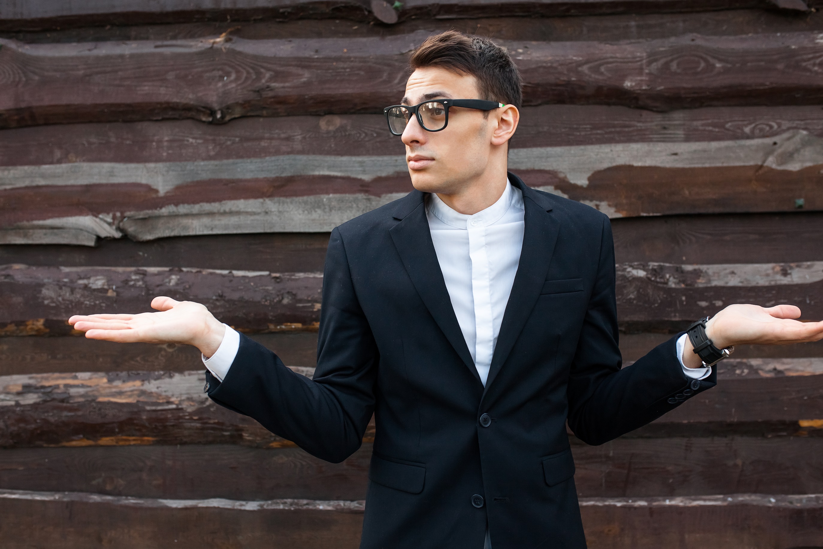 Surprised man wearing black suit with outstretched palms.