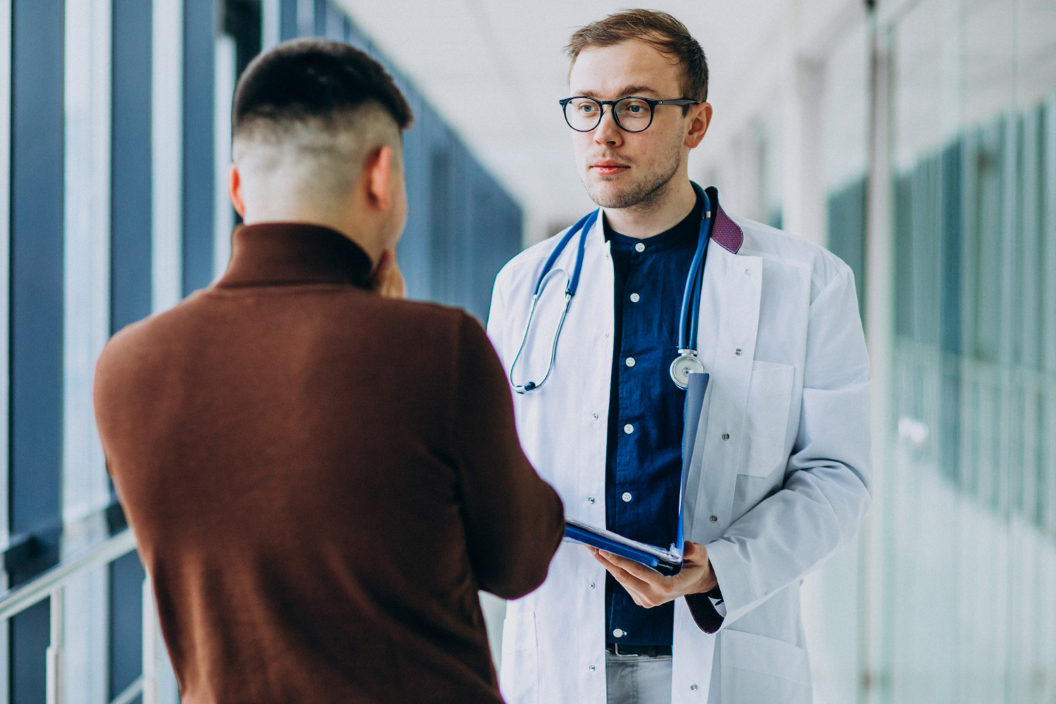 Young man is talking with a doctor in hospital hallway.