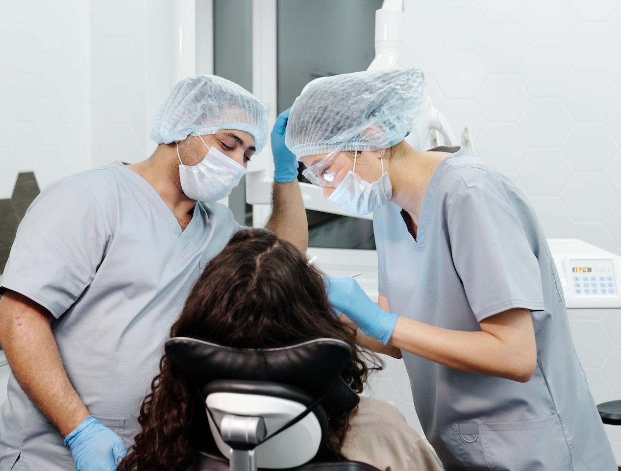 Woman seating on dentist chair with two dentists by her side.