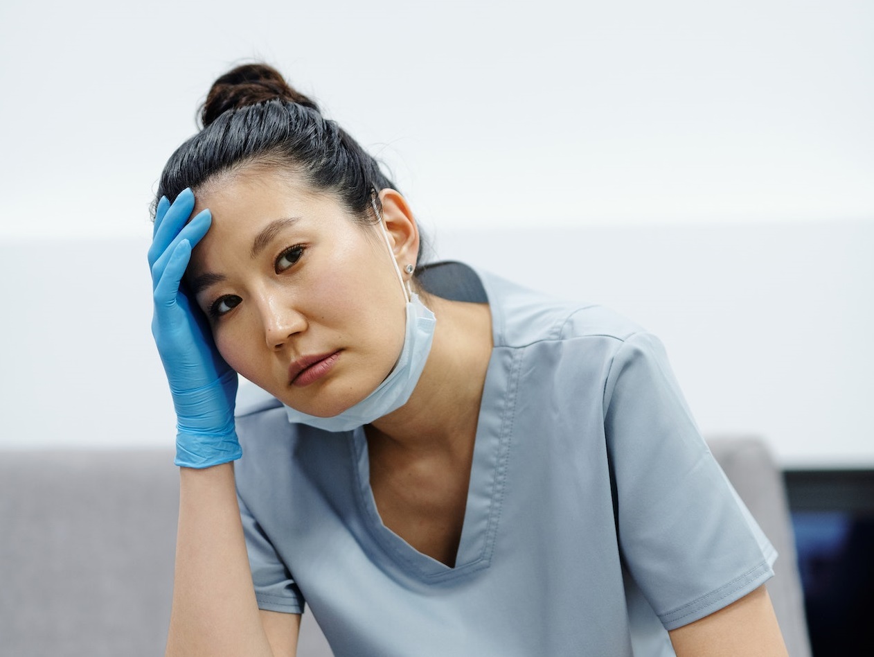 Young nurse wearing blue hospital clothes is seating worried.