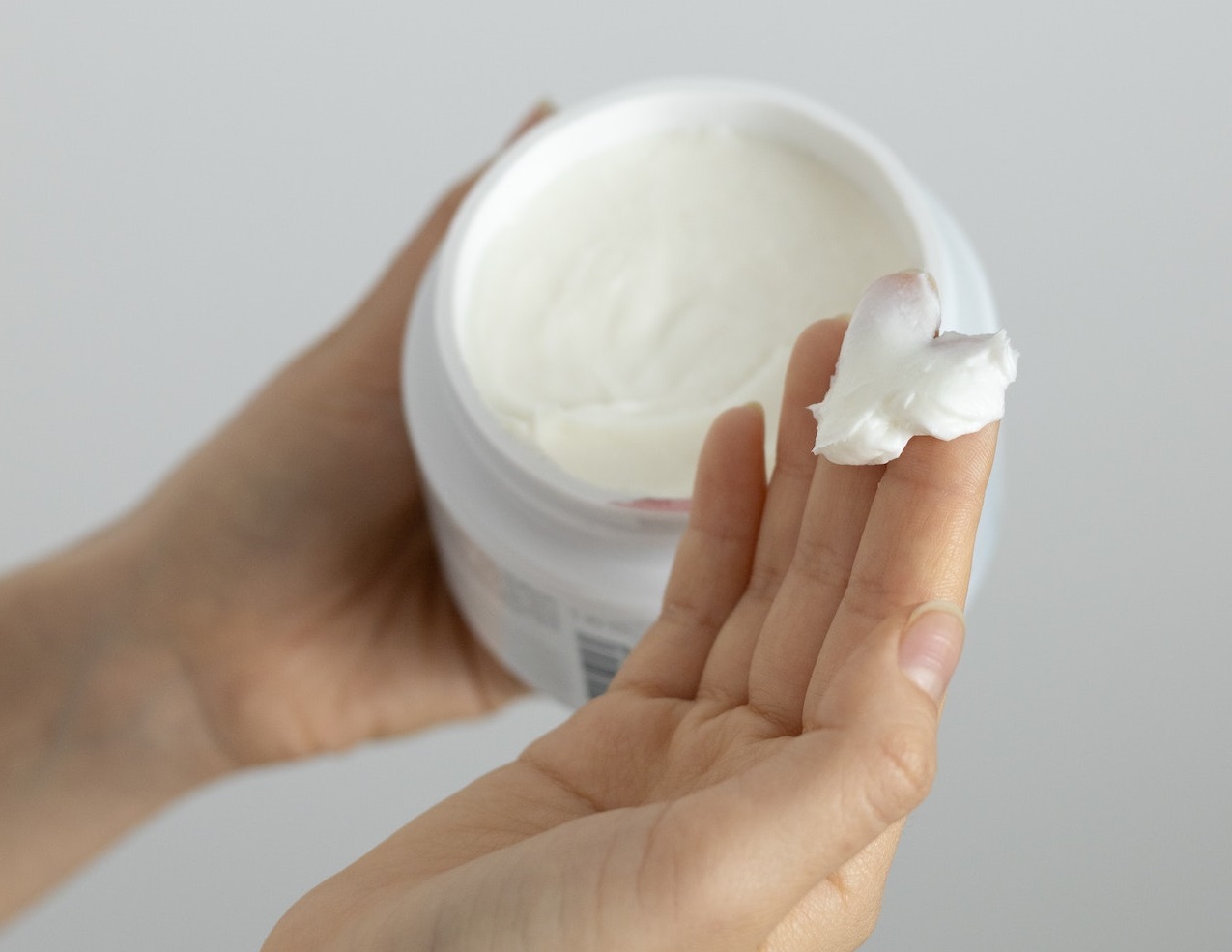 A person is holding a white cream in her hand.