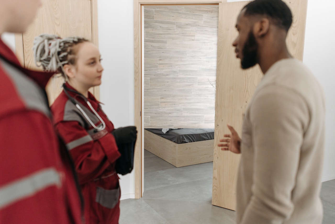 Man wearing brown sweater is talking with paramedics at home.