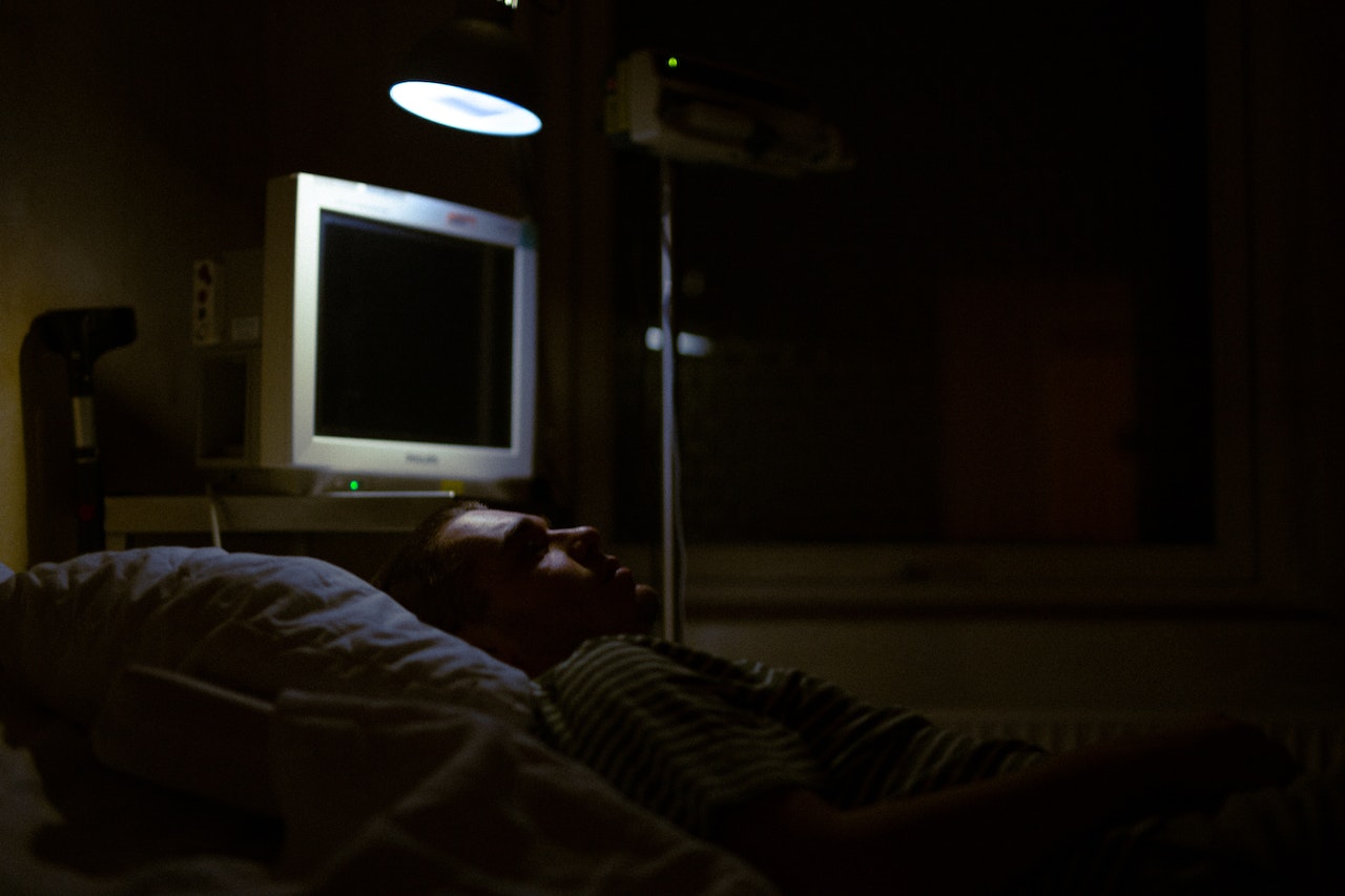 Male patient is laying in hospital bed in dark hospital room.