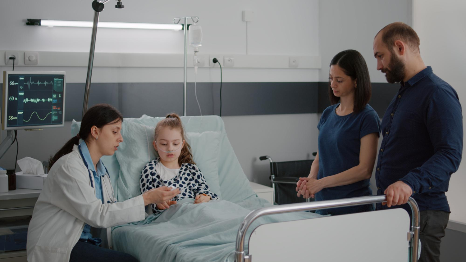 Little girl is seating in hospital bed with her parents and female doctor.