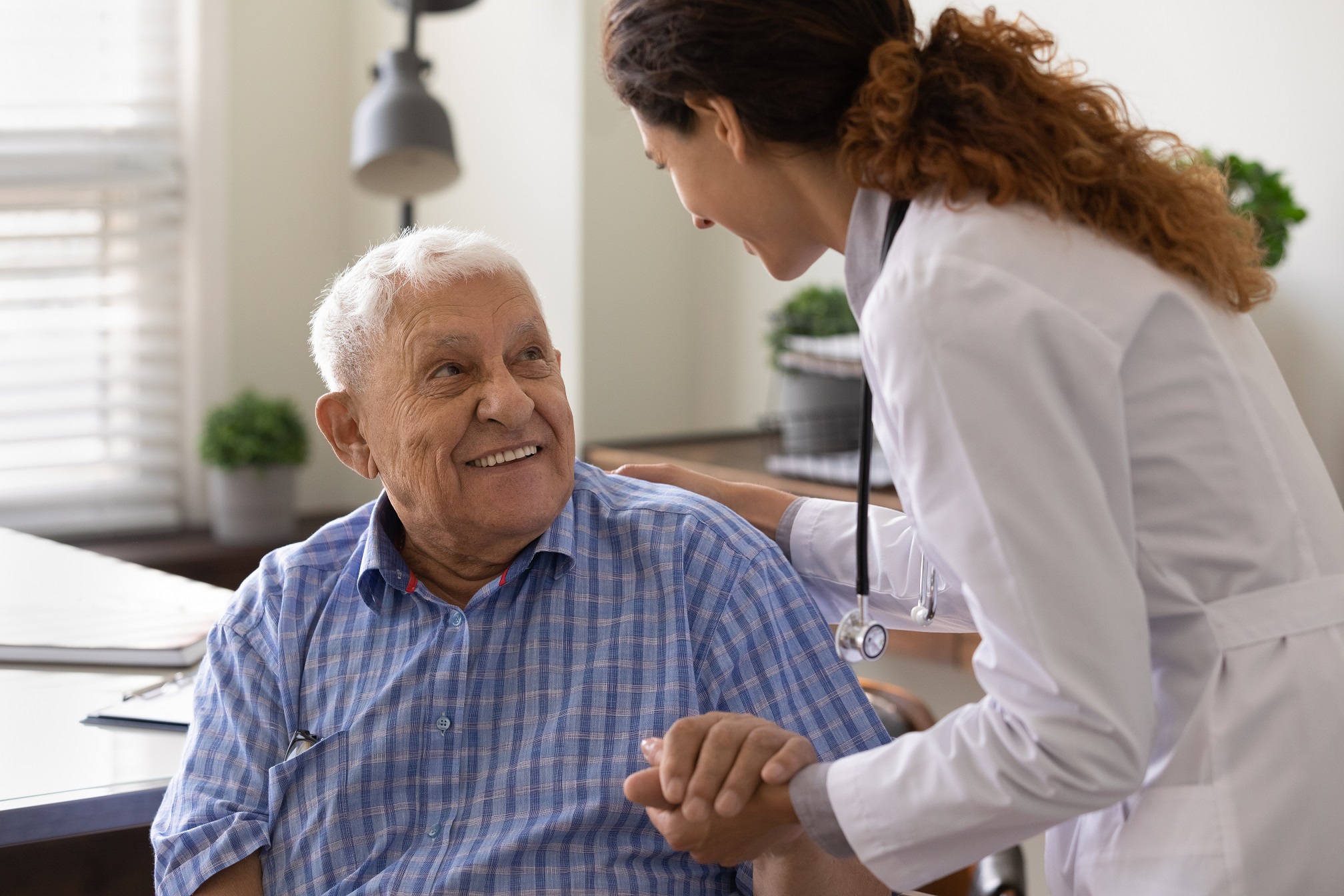 Caring nurse holding mature patient hand at meeting in hospital.