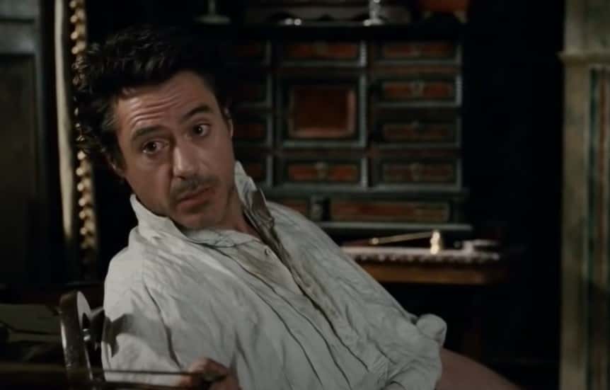 Robert Downey Jr in  Sherlock Holmes sitting on a chair in white shirt