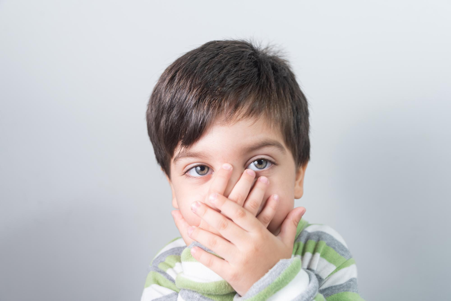 Small kid is covering his face with his hands