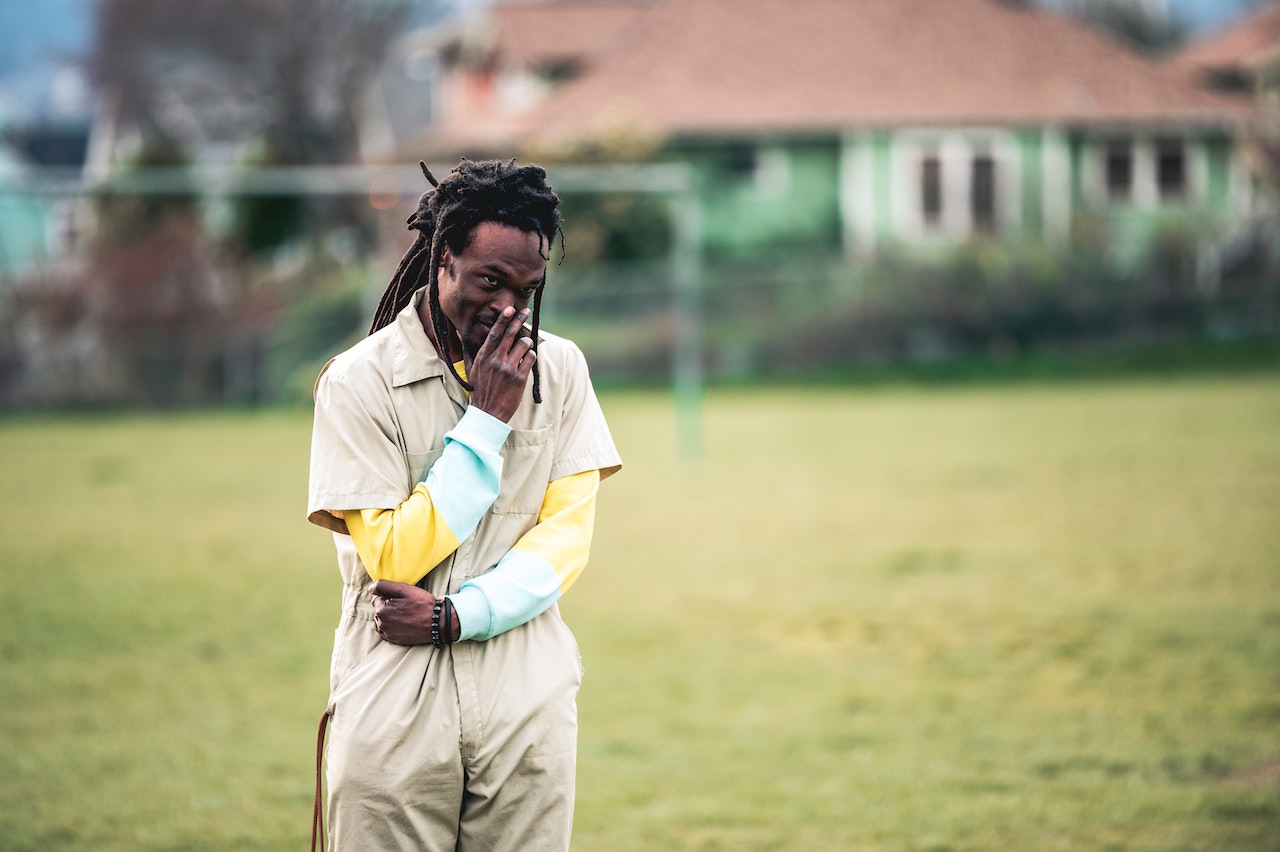 Young man is standing alone in the lawn outside.