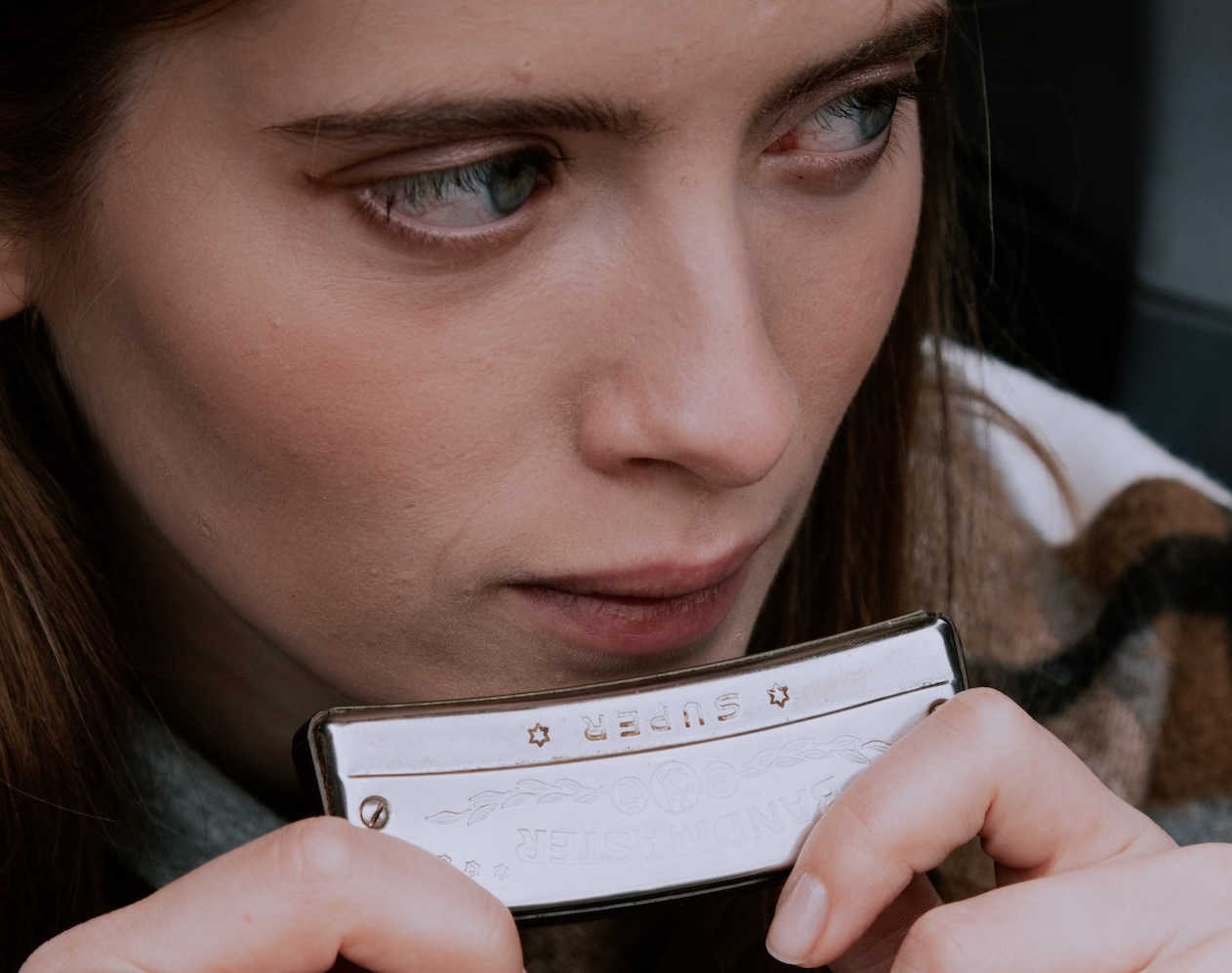 Young woman is playing on harmonica and looking at side.