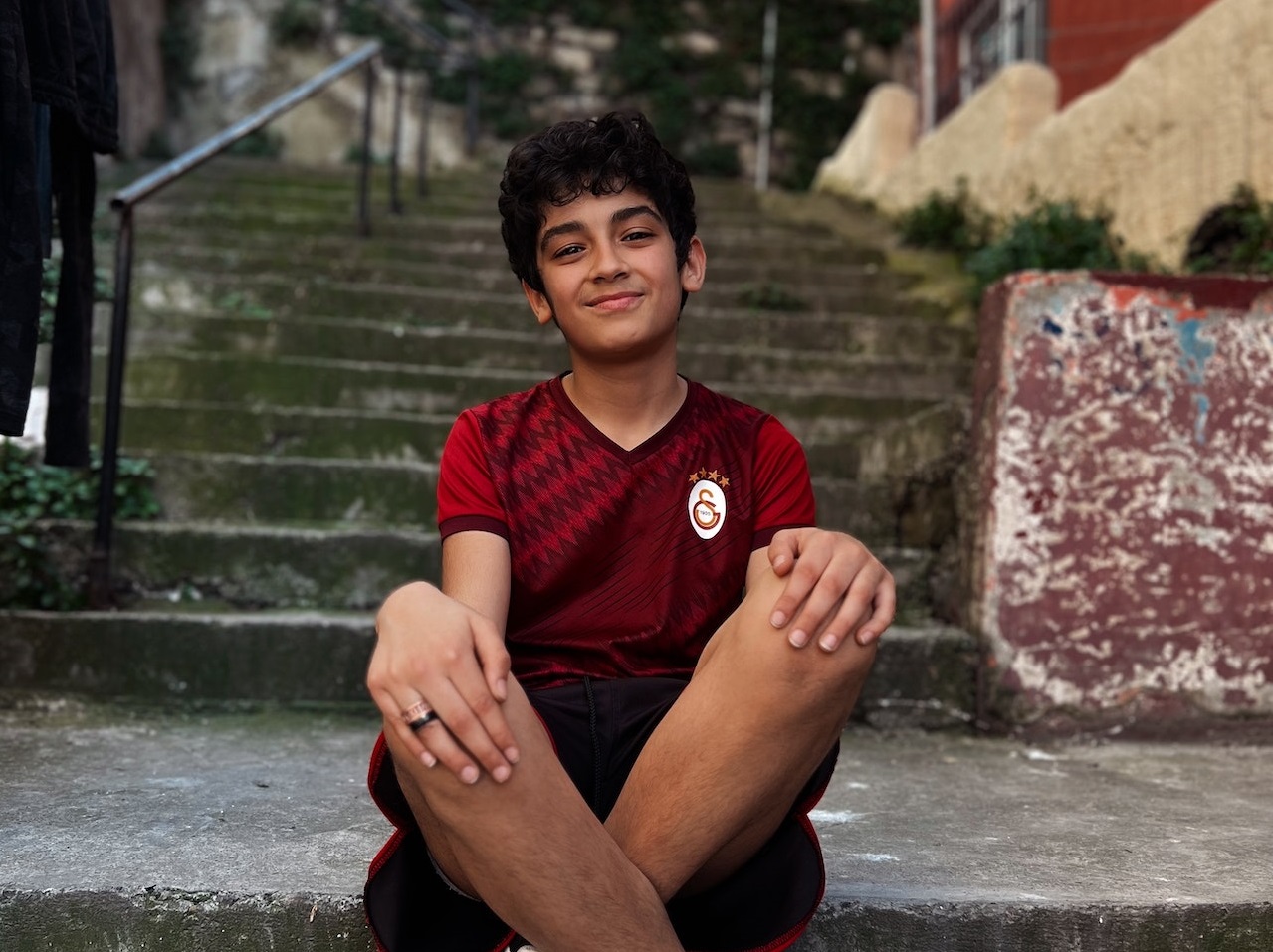 Young kid is seating outside on stairs ,looking at camera.