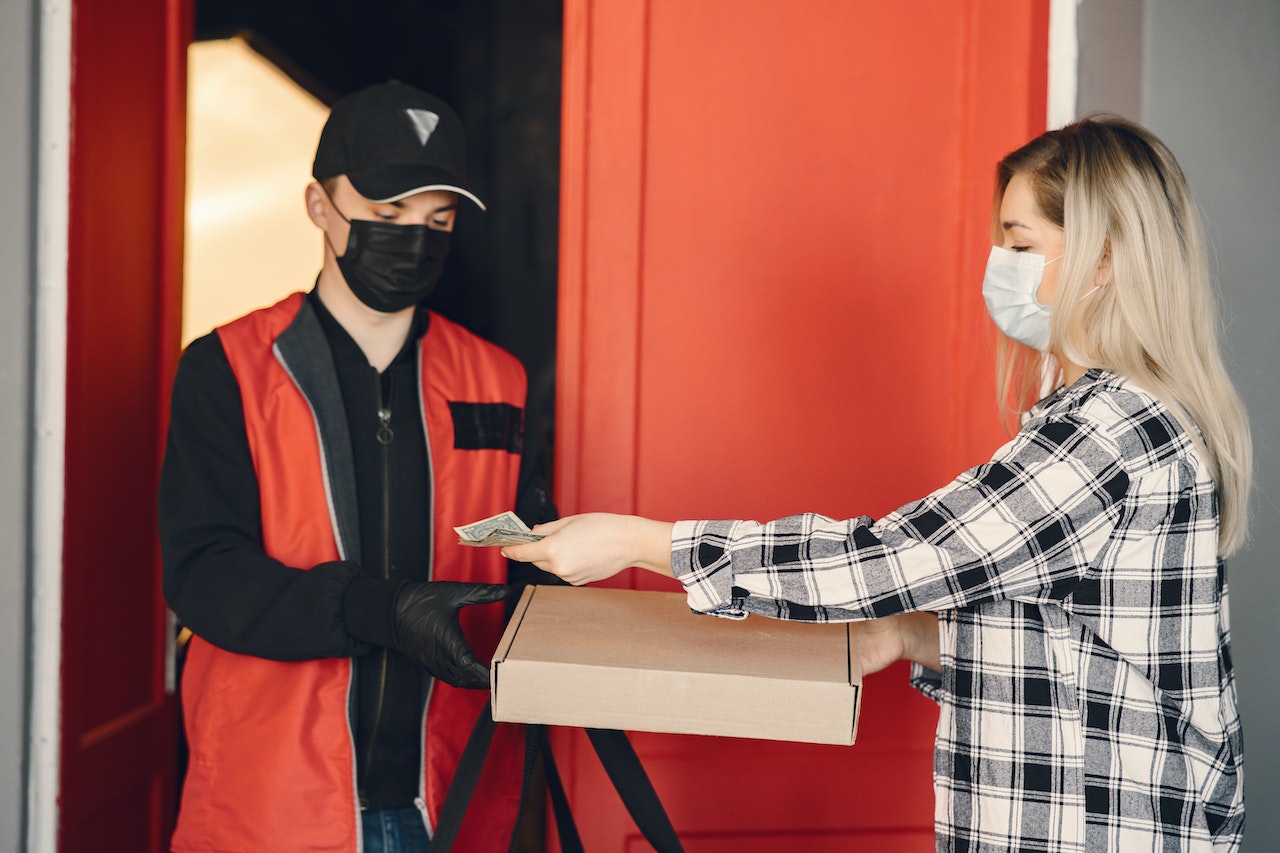 Man is delivering pizza to woman who is holding a money.