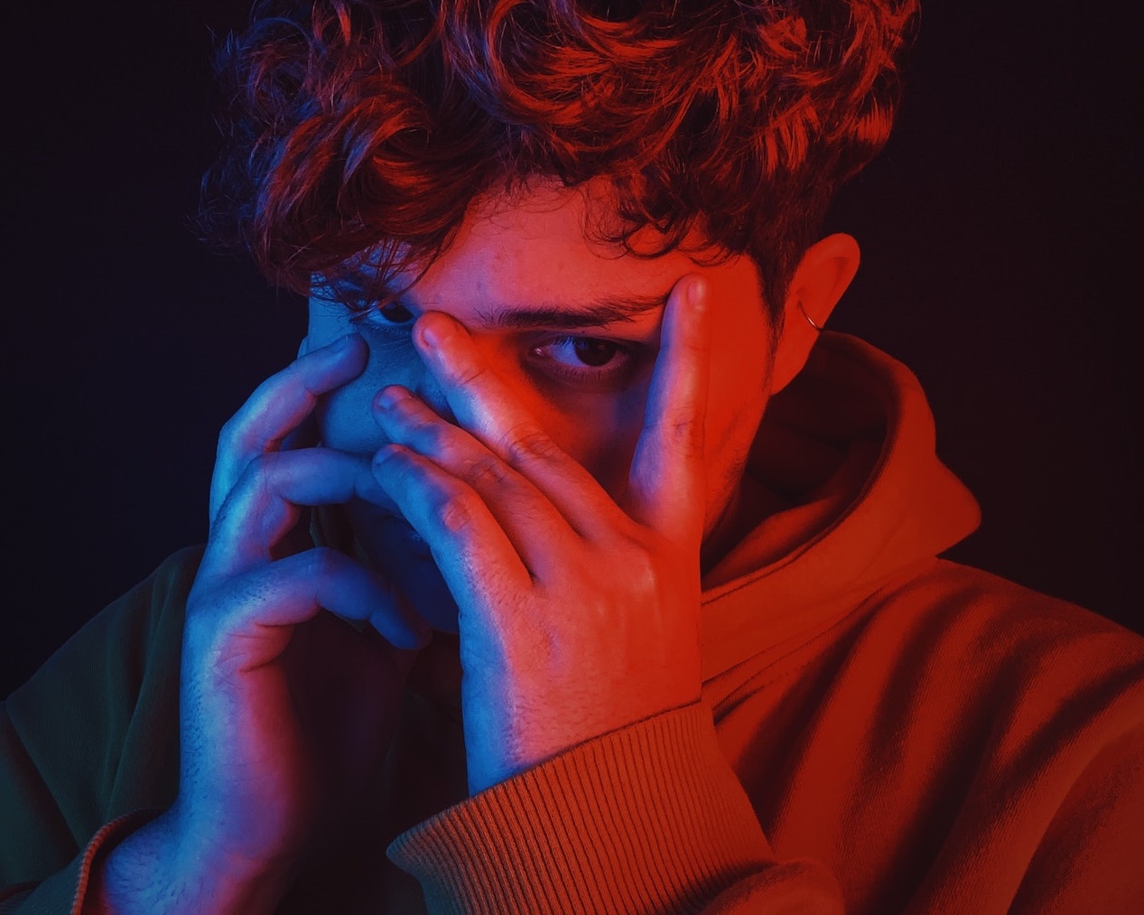 Young man wearing hoodie is hiding his face.