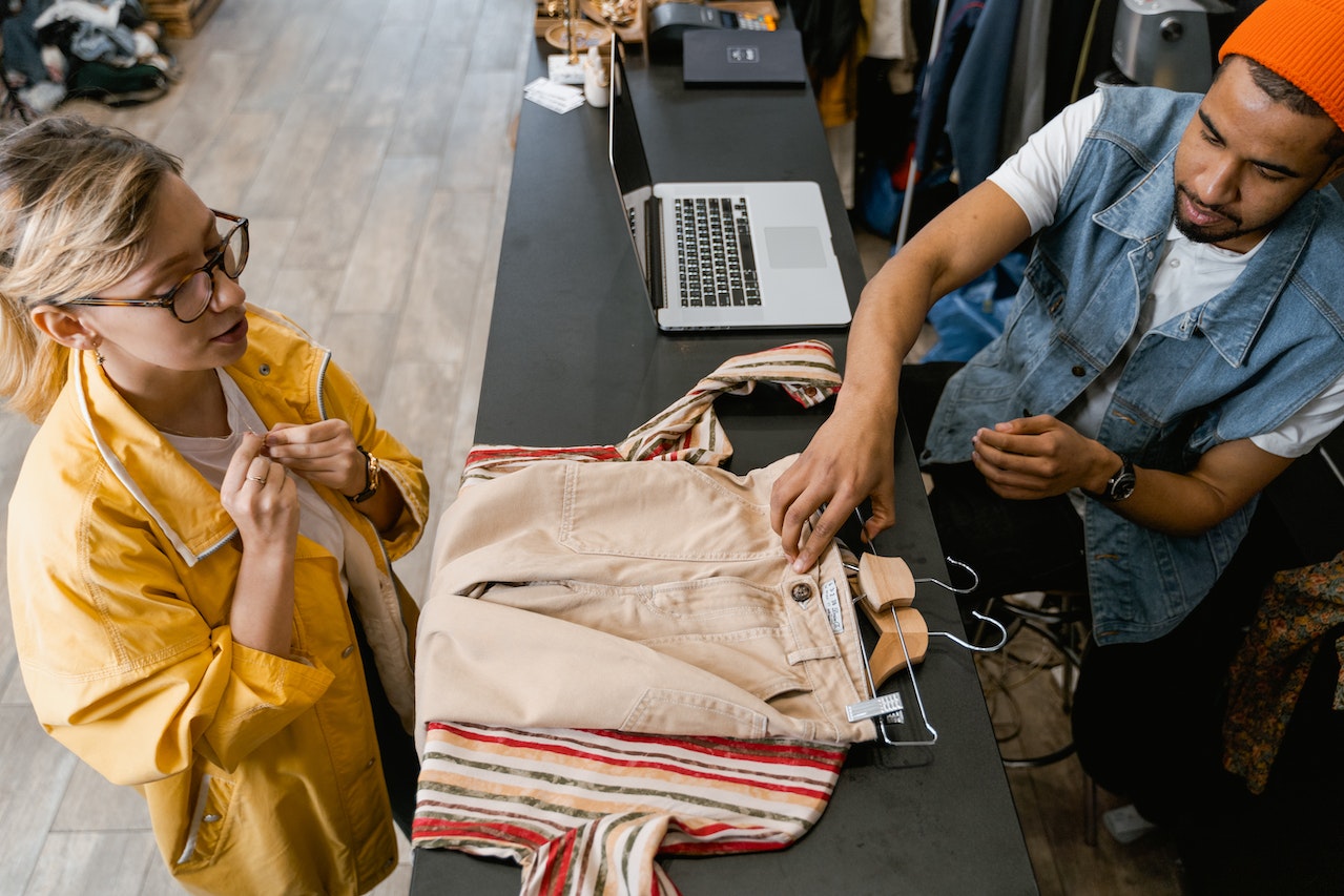 Man is selling clothes in store to a young woman in yellow jacket.
