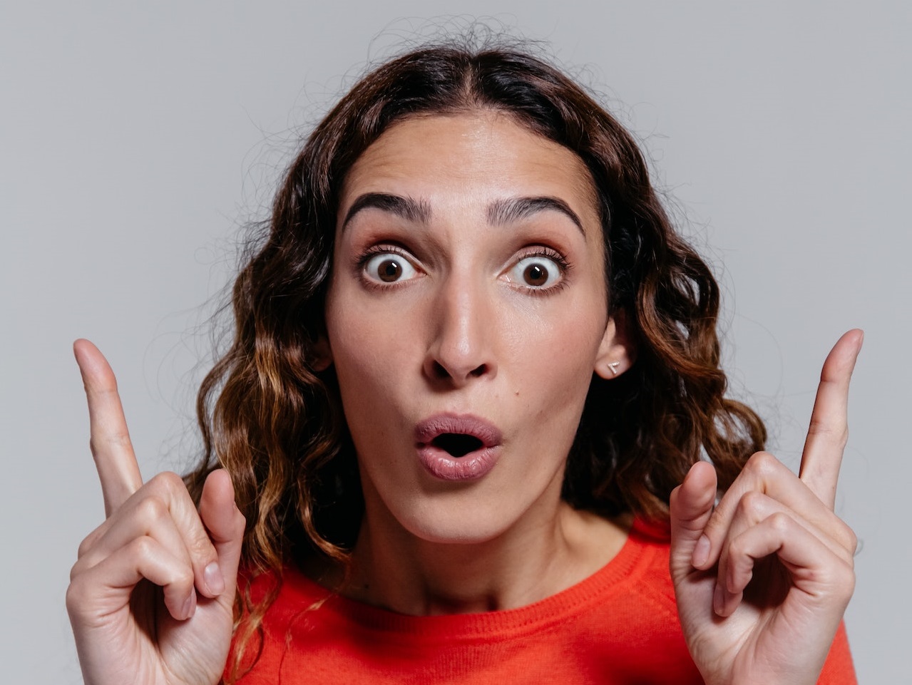 Young woman is pointing up and looking surprised.